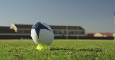 Genç, yetişkin, melez bir kadın rugby oyuncusunun ön tarafı topa doğru koşup tekme atıyor. 