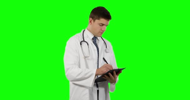若い白人男性医師の正面図は クリップボードを保持し カメラに微笑み グリーンスクリーンを書きます — ストック動画