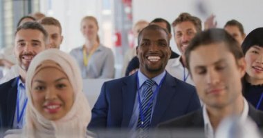 Bir iş seminerinde çeşitli gülümseyen izleyicilerin ön görüntüsünü kapatın. Hepsi sunumun sonunda soru sormak için ellerini kaldırıyor.