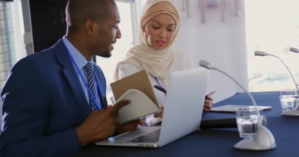 アフリカ系アメリカ人の若い実業家とアジア系の若い実業家がビジネス会議で隣に座っているヒジャーブを着てメモを取る — ストック動画