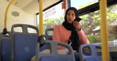 Bir şehirde bir otobüste oturan bir hijab commuting giyen genç bir karışık Yarış kadın ön görünümü, akıllı telefon konuşurken
