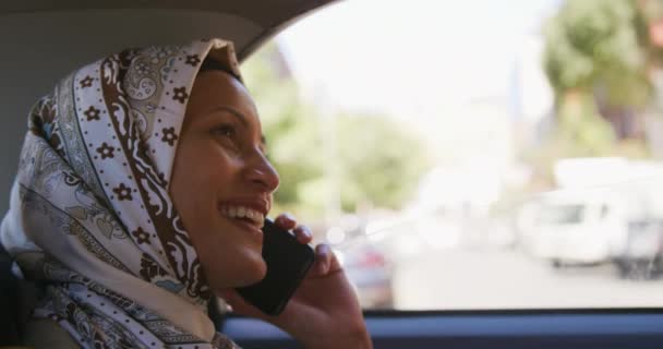 一个年轻的混血女人戴着头巾坐在一个城市的出租车上 在智能手机上说话 面带微笑的侧视图特写 — 图库视频影像