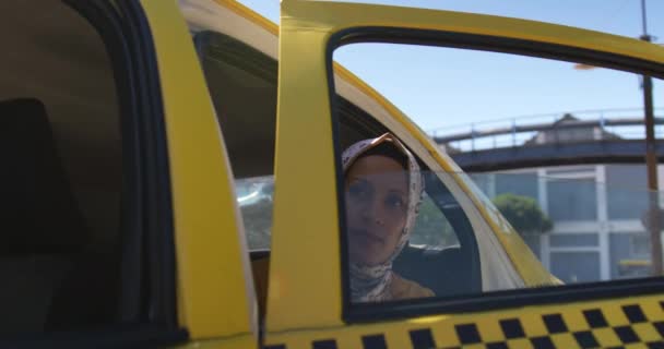 一个年轻的混血女人戴着头巾 从城市出租车里走出来的前视图 — 图库视频影像