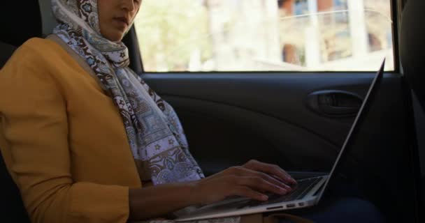 一个年轻的混血女人戴着头巾坐在一辆出租车上在城市驾驶的侧视图 在智能手机上发短信 — 图库视频影像