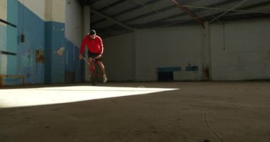 Terk edilmiş bir depoda hile yaparken güneş ışığı şaft bir Bmx bisiklet ön tekerlek üzerinde dengeleme genç bir Kafkas adam ön görünümü