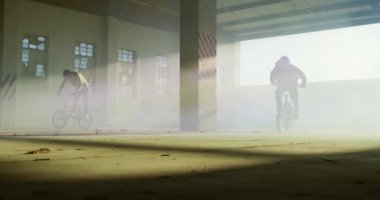 Terk edilmiş bir depoda, mavi ve sarı sis bombaları ile Bmx bisiklet sürme ve hile yapıyor iki genç Kafkas erkeklerin ön görünümü