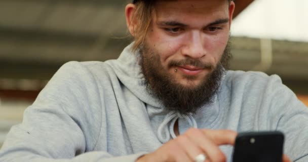 一个年轻的成年白种人男子坐在一个废弃的仓库里坐着 用智能手机的特写镜头 — 图库视频影像