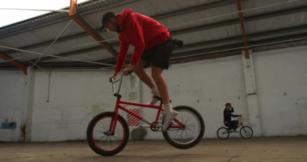 버려진 창고에서 트릭을 연습하는 Bmx 자전거의 바퀴에서 남자의 측면보기 — 비디오