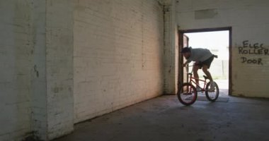 Terk edilmiş bir depoda Bmx bisikletine binen beyaz bir adamın ön görünümü