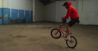 Terk edilmiş bir depoda Bmx motoruyla hoplayıp zıplayan beyaz bir adamın yan görüntüsü.