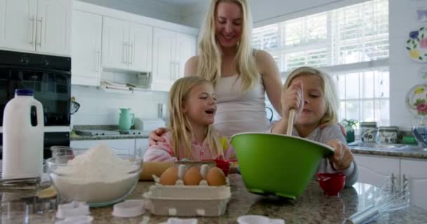 圣诞节前夕 一位快乐的白人年轻母亲带着年幼的女儿和儿子在厨房里做饼干 在搅拌的碗里搅拌配料 互相望着对方 这让人眼前一亮 — 图库视频影像