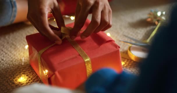 圣诞节那天 一位混血儿的母亲和她的小女儿坐在客厅的地板上 用红纸把礼物包在一起 用金丝带捆起来 — 图库视频影像
