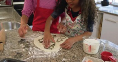 Noel 'de küçük kızıyla mutfakta melez bir annenin kurabiye yaparken, hamuru kesiciyle şekillendirirken ve birbirlerine gülümserken ön cephe görüntüsü.