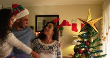 Noel 'de küçük kızlarıyla oturma odalarında oturan melez bir ailenin yan görüntüsü. Adam Noel Baba şapkası takıyor ve kızını kucağında tutuyor.