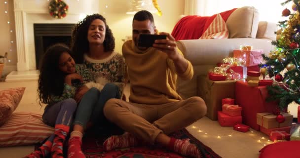 クリスマスの間に若い娘と一緒に座って床に座り お父さんはスマートフォンでセルフィーを撮る — ストック動画