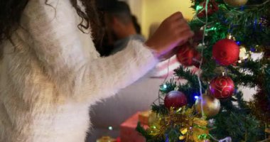 Noel 'de oturma odasında Noel ağacını süsleyen ve arka plandaki şöminenin yanında babasının yanına oturmak için koşan melez bir kızın yan görüntüsü.