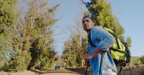 田舎の太陽の下でのトレッキング中にリュックサックと一緒に歩く若い混合レースの男の側面図 — ストック動画