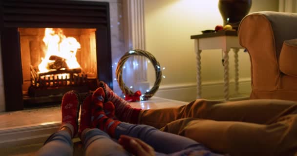 クリスマスには暖炉のそばの床に横になって足を暖めながら座っています — ストック動画