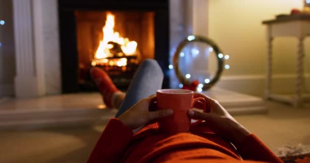 圣诞节时 一位混血儿躺在客厅里 躺在壁炉前 暖着脚 在杯子里端着一杯热饮 低矮地望着她 — 图库视频影像