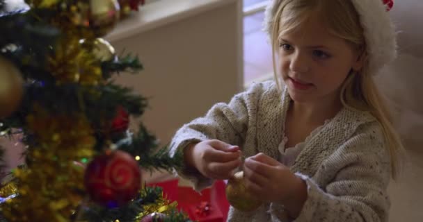 一个笑容可亲的白人女孩头戴圣诞帽 装饰着客厅里的圣诞树 — 图库视频影像
