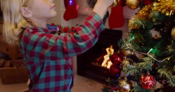 若い白人の男の子のサイドビュークリスマスの時間に赤ちゃんと彼のシッティングルームでクリスマスツリーを飾る — ストック動画