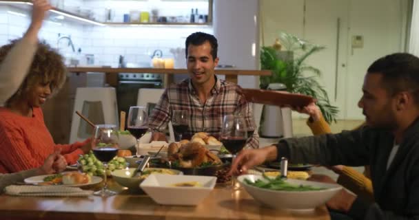 一群年轻的 多民族的男女朋友围坐在桌旁聊天 在家里互相招待感恩节大餐 举杯庆祝一番 — 图库视频影像