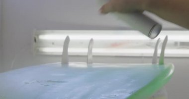 Atölyesinde çalışan bin yıllık beyaz erkek sörf tahtası yapımcısının elini kapayarak bir sörf tahtası boyuyor.