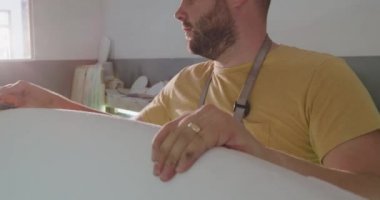 Bin yıllık beyaz bir erkek sörf tahtası üreticisinin atölyesindeki ön görüntüsü üretim sürecinde yeni bir sörf tahtası cilalıyor.