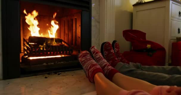 Nízká část nohou bělošského páru ležícího na podlaze a ohřívajícího si nohy u otevřeného krbu v krbu v obývacím pokoji o Vánocích