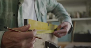 Kafkasyalı bir adamın evdeki bir atölyede Diy 'i çekerken yan görüntüsü. Ahşabı mezura ile ölçüyor ve yavaş çekimde kalemle işaretliyor.