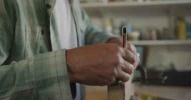 Yan görüntüde, gözlüklü beyaz bir adam evdeki bir atölyede Diy taklidi yapıyor, mezura ile ölçüyor ve bir ahşap parçasını kalem ile kıskaçlıyor, yavaş çekim.