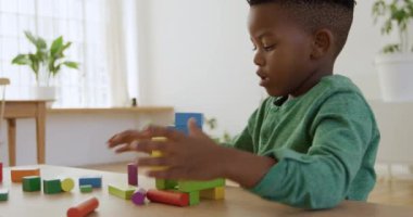 Yan görüntü, genç bir Afrikalı Amerikalı çocuğun evdeki masada yapı taşlarıyla oynaması, yavaş çekim.