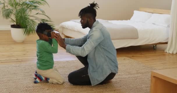 彼の若い息子が自宅の寝室でVrヘッドセットを使用するのを助ける100万人のアフリカ系アメリカ人の父親の側面図 — ストック動画