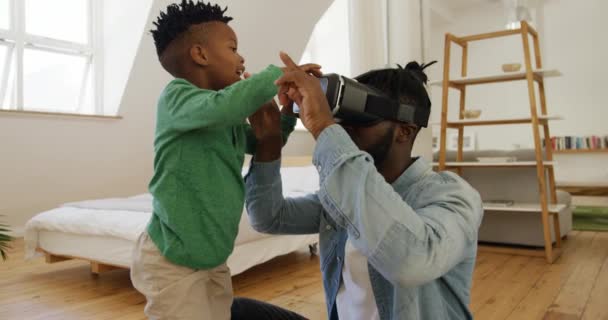 彼の千年の父を助ける若いアフリカ系アメリカ人少年のサイドビュー自宅の寝室でVrヘッドセットを使用します スローモーション — ストック動画