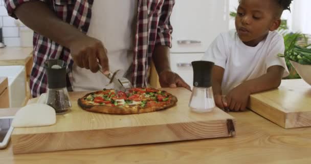 一个千禧年的非洲父亲和他年幼的儿子在厨房里一起做饭聊天 父亲一边切披萨 一边看着儿子慢吞吞地走着 — 图库视频影像