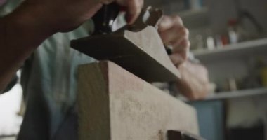 Kafkasyalı bir adamın evdeki bir atölyede Diy 'i çekerken yan görüntüsü, ahşap bir parçayı yavaş çekimde mengeneye sıkıştırıyor.