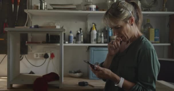 白人女性の側面図自宅でのワークショップで死ぬ 家具の一部に取り組んで スマートフォン スローモーションを使用して — ストック動画