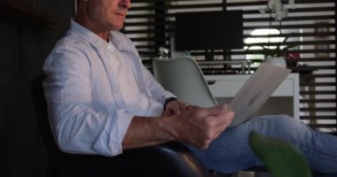 Kafkasyalı bir adamın, evde dizüstü bilgisayar kullanırken, karanlık bir odada, sandalyede otururken yan görüntüsü.