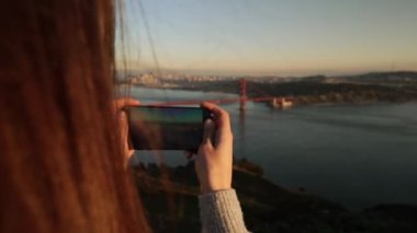 Golden Gate Ulusal Rekreasyon Bölgesi 'nde dikilen beyaz saçlı genç bir kadının arka görüntüsü. Golden Gate Köprüsü ve San Francisco Körfezi bölgesinin resimlerini çekiyor. Akıllı telefonuyla, ağır çekimde.