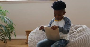 Afro-Amerikalı genç bir çocuğun evde sessizce oturduğu bir çantanın üzerinde tablet bilgisayar kullanarak ağır çekimde