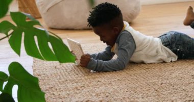 Evde, tablet bilgisayar kullanarak yerde sessizce yatan Afrikalı Amerikalı genç bir çocuğun yan görüntüsü.