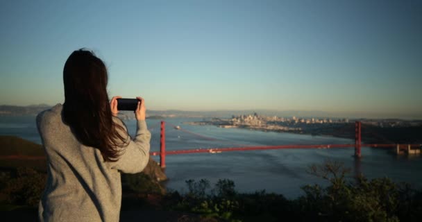 一个白种人的年轻女子站在金门国家娱乐区 拿着智能手机拍摄金门大桥和旧金山湾区的照片 — 图库视频影像