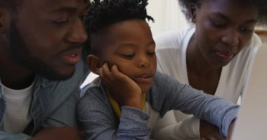 Binlerce yıllık gülümseyen Afro-Amerikan ailesinin ve genç oğullarının dizüstü bilgisayar kullanarak ve ağır çekimde konuşarak yatakta yan yana yatışının ön görüntüsü.