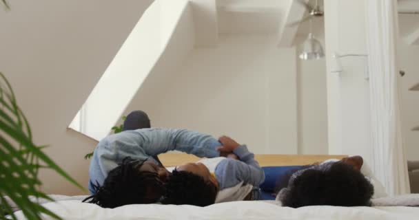 彼の息子と一緒に家で遊んでいる彼のベッドの上に横たわっ千年のアフリカ系アメリカ人の父親のフロントビュー スローモーション — ストック動画