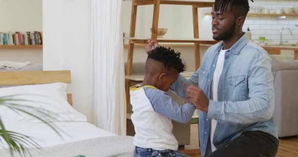 一个千禧年的非洲父亲帮他的小儿子在家里换衣服和他说话的侧视图 — 图库视频影像