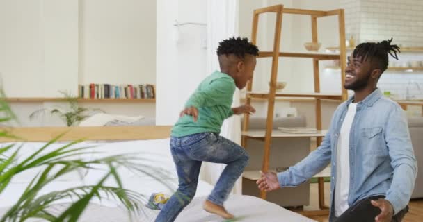 彼の千年の父の腕の中に飛び込む彼の家でベッドの上に立っている若いアフリカ系アメリカ人の少年の側面図 — ストック動画