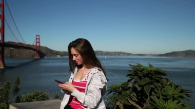 San Francisco Körfez Bölgesi 'nde Golden Gate Köprüsü' nün yanında uzun siyah saçlı, gülümseyen beyaz bir kadının görüntüsü.