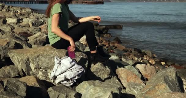 一个黑头发的女人坐在水边的岩石上 用智能手机与金门大桥和旧金山湾地区合影 — 图库视频影像