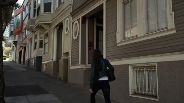 女性の後ろのビューには ツリーで丘を歩いてハンドバッグを運ぶ 住宅街の通り並ぶ スローモーションで — ストック動画