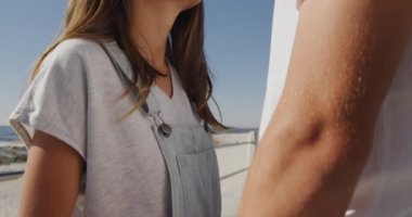 Mutlu, genç, beyaz bir çiftin deniz kenarında el ele tutuşup, başlarını okşayarak, gülümseyerek, ağır çekim